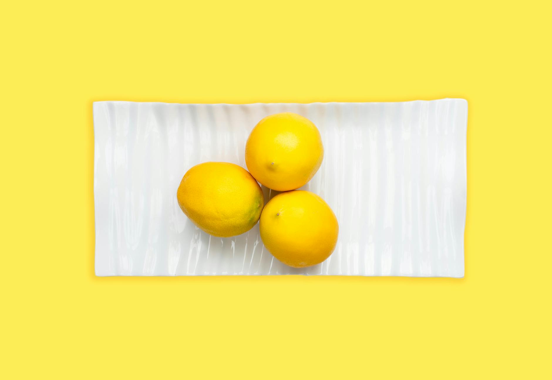 Fresh lemons on a white plate with a vibrant yellow background, symbolizing renewal and authentic self-expression