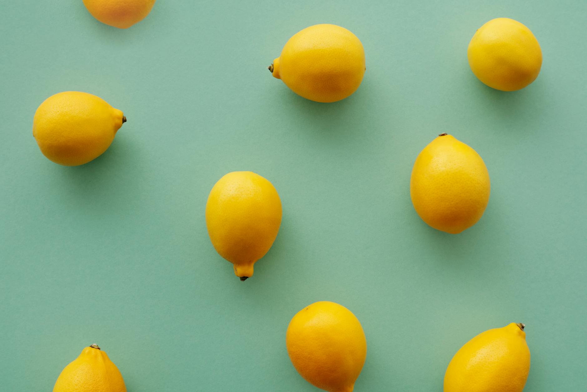 Bright yellow lemons arranged on a pastel green background, creating a fresh and vibrant flat lay composition.