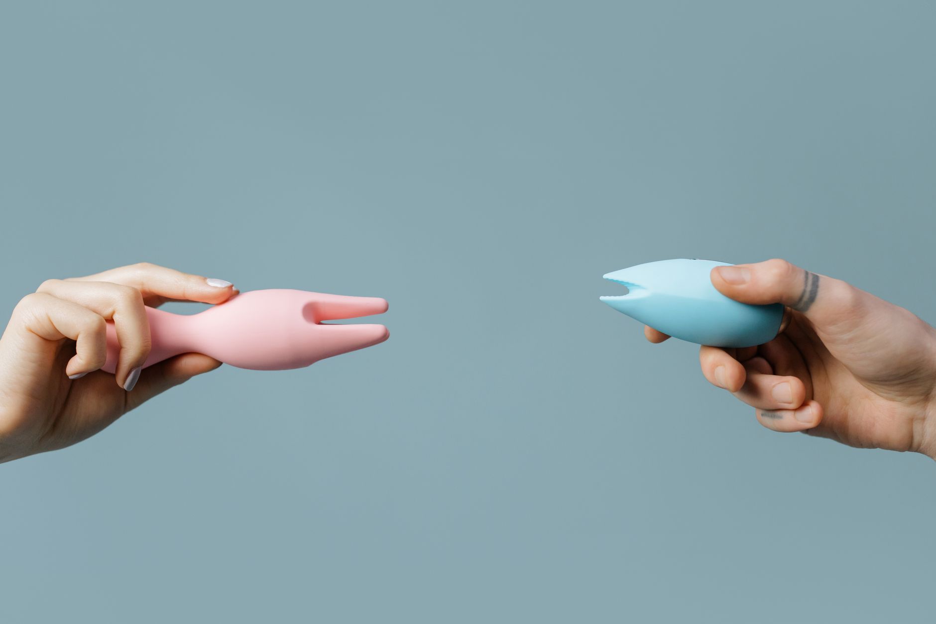 Two hands holding pink and blue silicone lemon vibrators against a pastel background