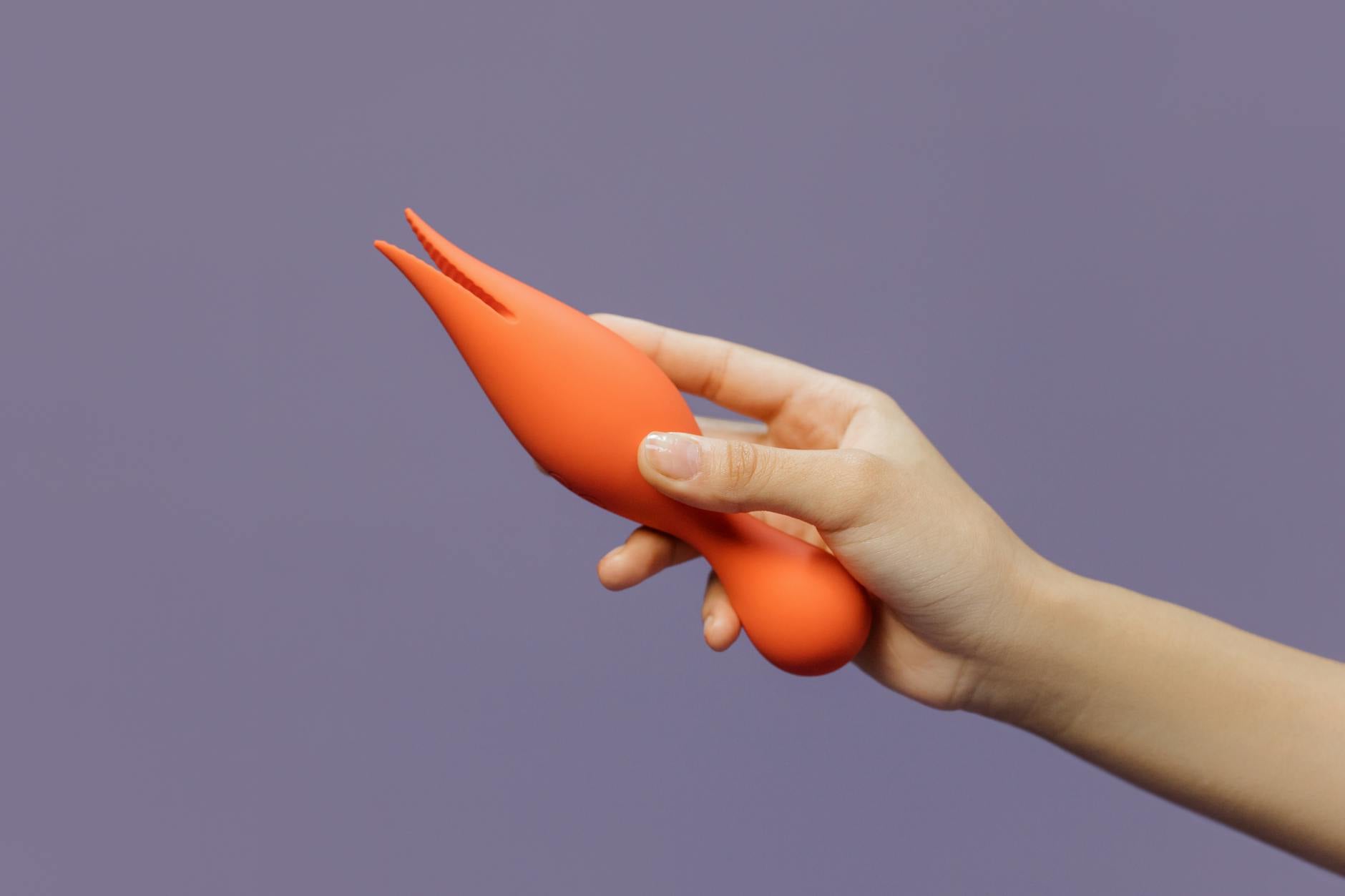 A close-up of a hand holding a vibrant orange lemon vibrator, demonstrating the tactile experience of sensual exploration