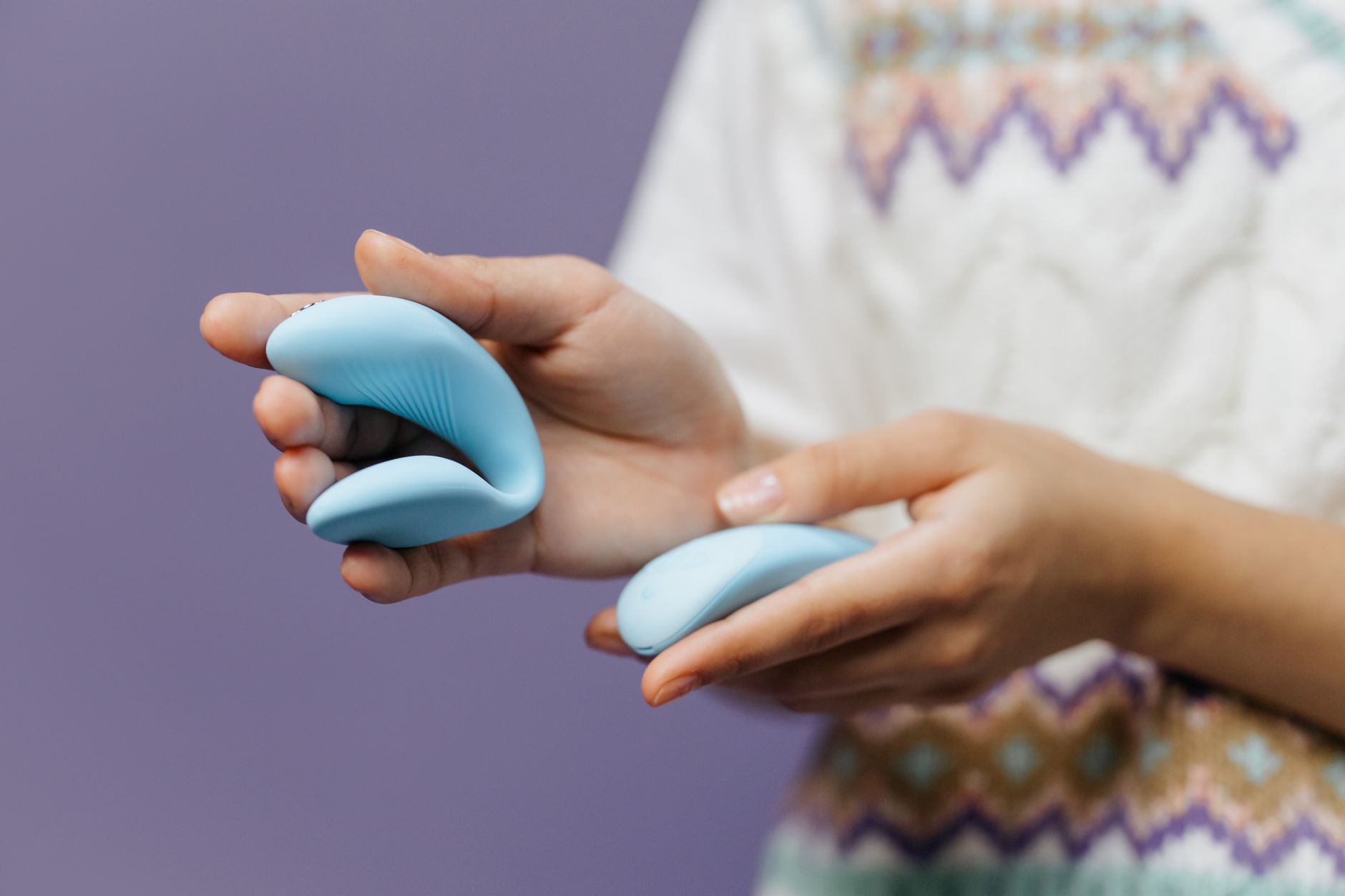 Hand holding a sleek blue lemon clitoral vibrator against a purple background