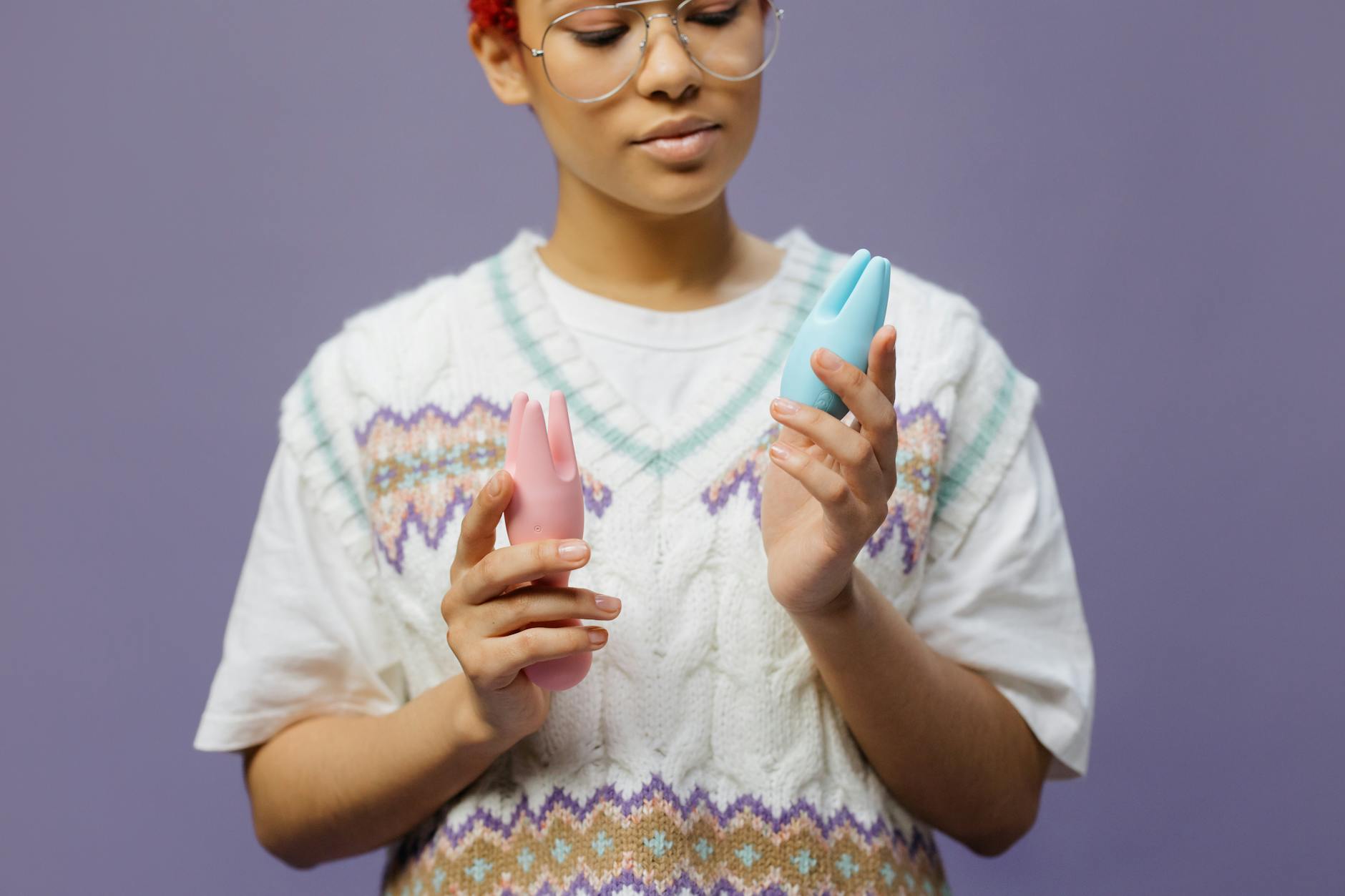Woman holding colorful vibrators thoughtfully against a contemplative background.