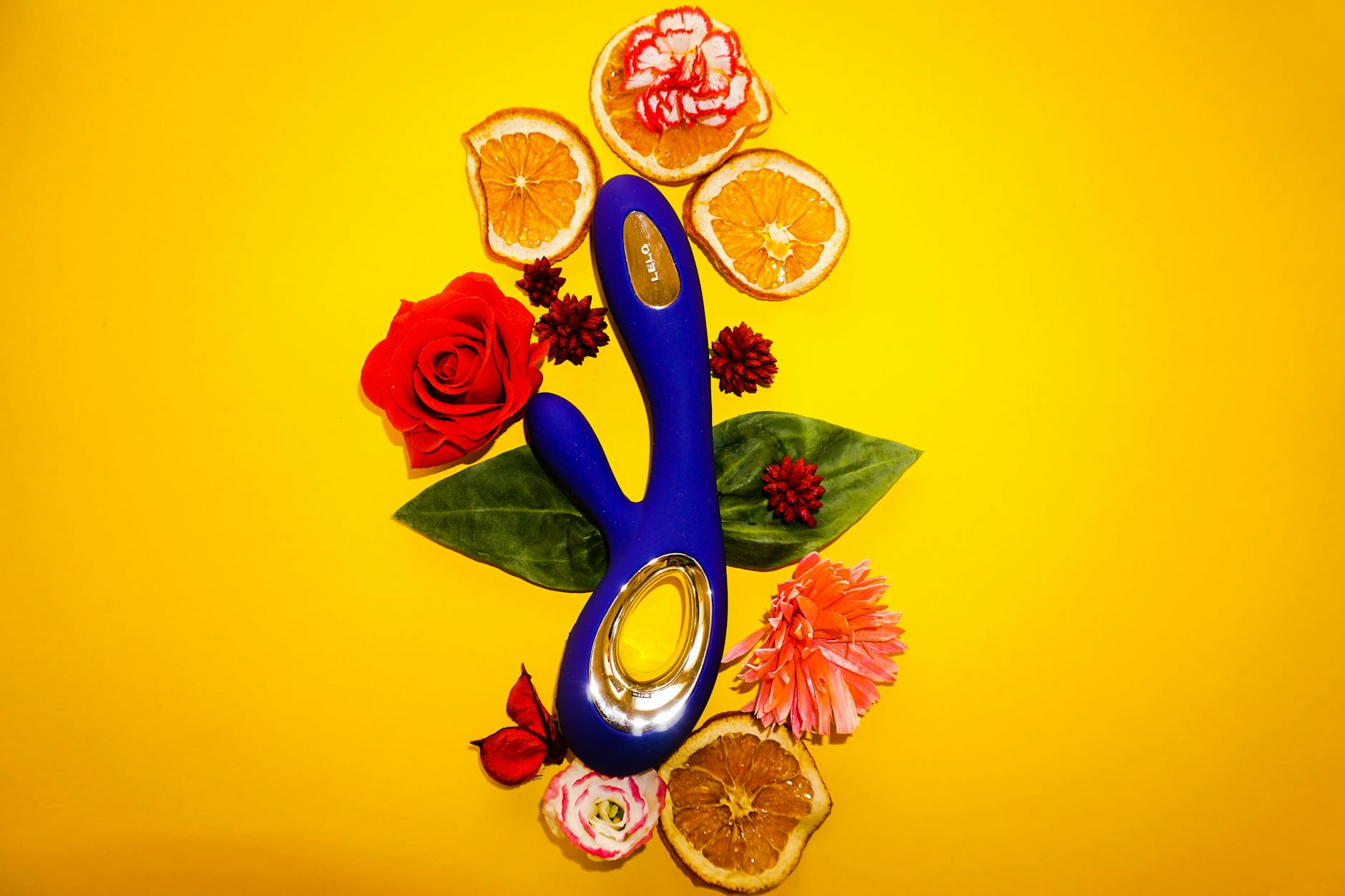 Blue lemon clitoral vibrator surrounded by fresh citrus and flowers on a bright yellow background