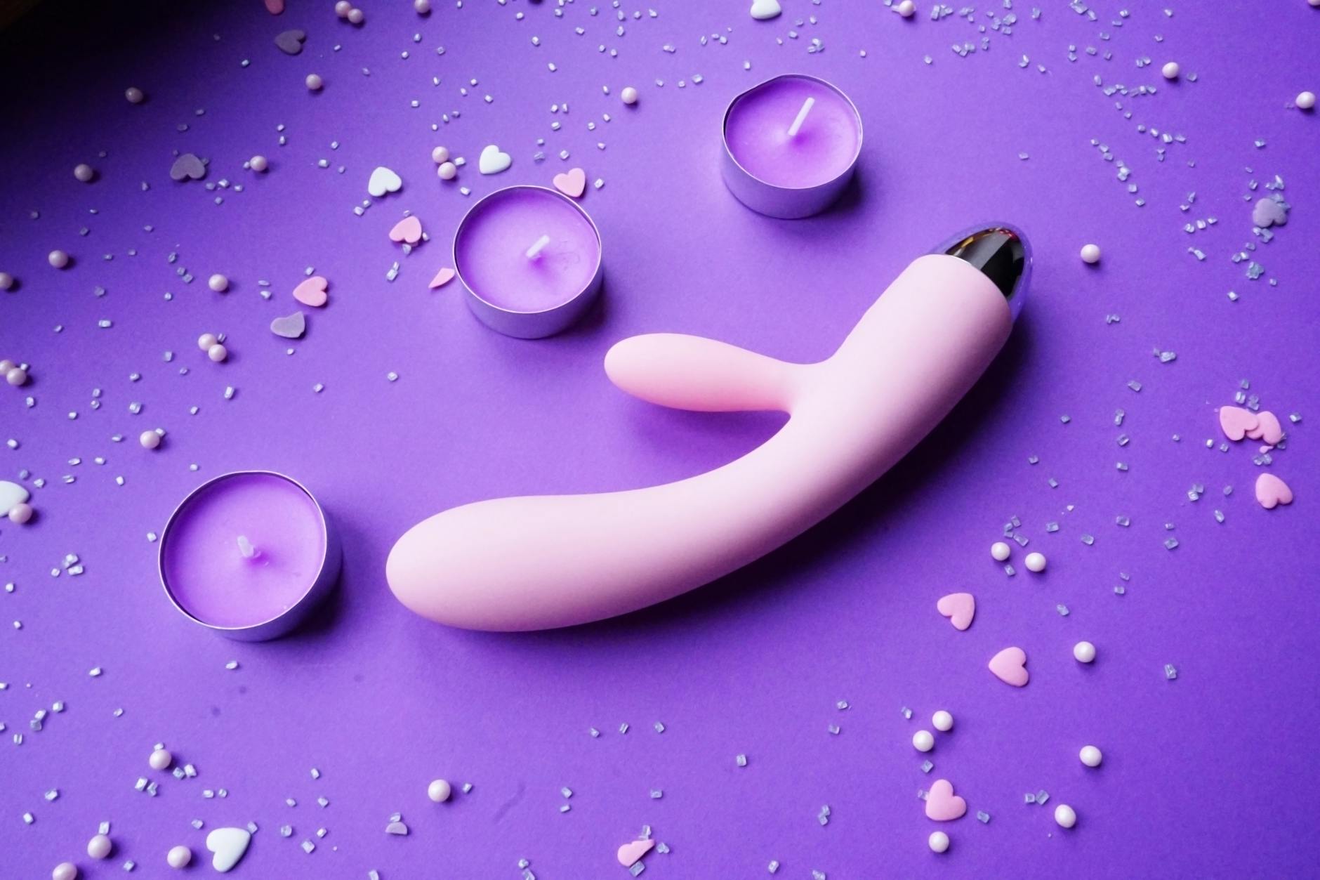 Pink lemon vibrator on purple background with candles and heart confetti